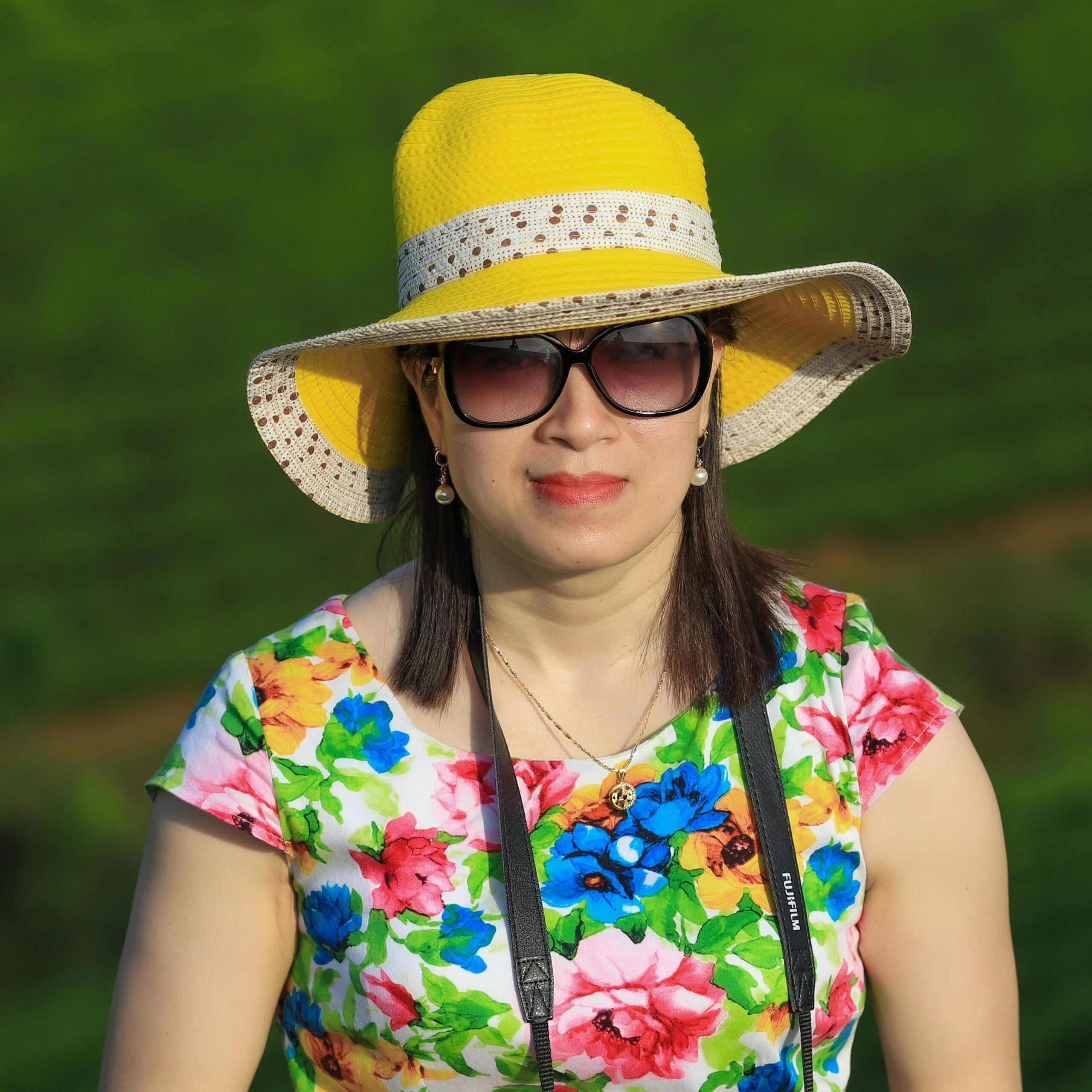 A woman wearing a floral dress and yellow hat stands in the vibrant tea fields of Phú Thọ, Vietnam.